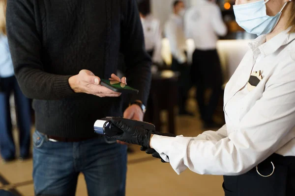 Restoranda NFC 'nin telefonuyla irtibat kurmadan para ödeyen bir adam. Koruyucu maske takan ve elinde kredi kartı okuyucu maskesiyle siyah eldivenler tutan bir kasiyer. Yeni normal kavram