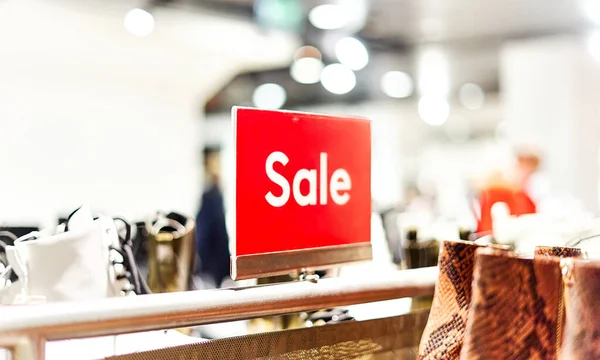 Ayakkabı ve aksesuarlarla çevrili bir kadın giyim mağazasında kırmızı, parlak bir satış tabelası. Perakende alışveriş merkezinde sezonluk indirim teklifi