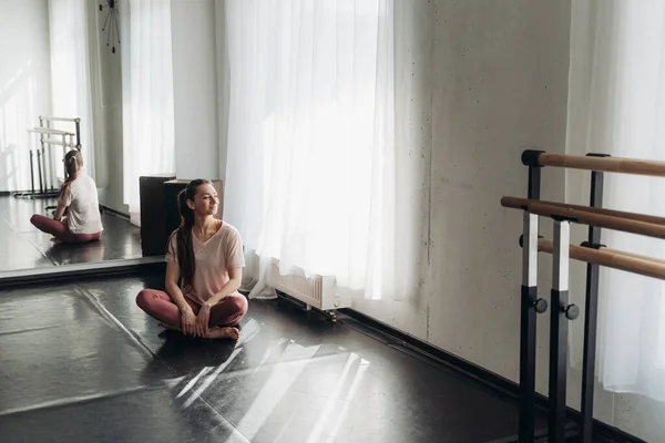 Pembe spor giyimli güzel, mutlu bir kadın başarılı bir spor salonundan sonra dinleniyor ya da dans sınıfında yerde oturuyor. Eğitimden sonra keyifli bir yorgunluk. Sağlıklı yaşam tarzı. Kopyalama alanı 