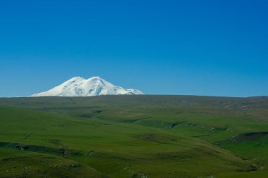 Güneşli bir günde, karlı Elbrus Dağı manzaralı güzel dağlık çayırlar.