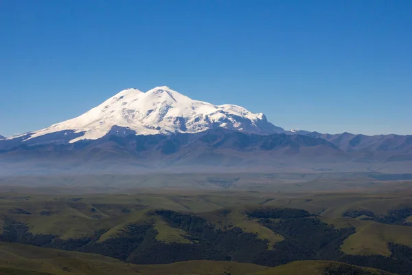 Platodan sönmüş volkana ve Elbrus Dağı 'nın karlı zirvesine mükemmel bir manzara. Aşağıda yeşil bir vadi var.