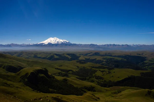 Platodan sönmüş volkana ve Elbrus Dağı 'nın karlı zirvesine mükemmel bir manzara. Aşağıda yeşil bir vadi var.