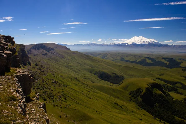 Platodan sönmüş volkana ve Elbrus Dağı 'nın karlı zirvesine mükemmel bir manzara. Aşağıda yeşil bir vadi var.