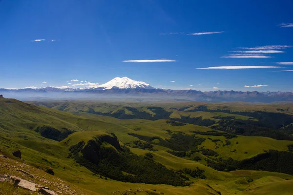 Platodan sönmüş volkana ve Elbrus Dağı 'nın karlı zirvesine mükemmel bir manzara. Aşağıda yeşil bir vadi var.
