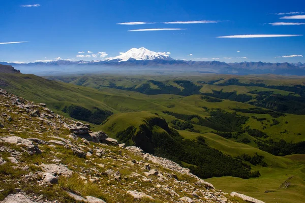 Platodan sönmüş volkana ve Elbrus Dağı 'nın karlı zirvesine mükemmel bir manzara. Aşağıda yeşil bir vadi var.