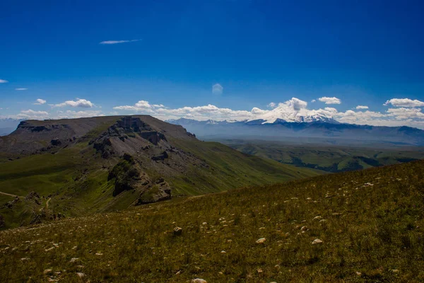 Platodan sönmüş volkana ve Elbrus Dağı 'nın karlı zirvesine mükemmel bir manzara. Aşağıda yeşil bir vadi var.