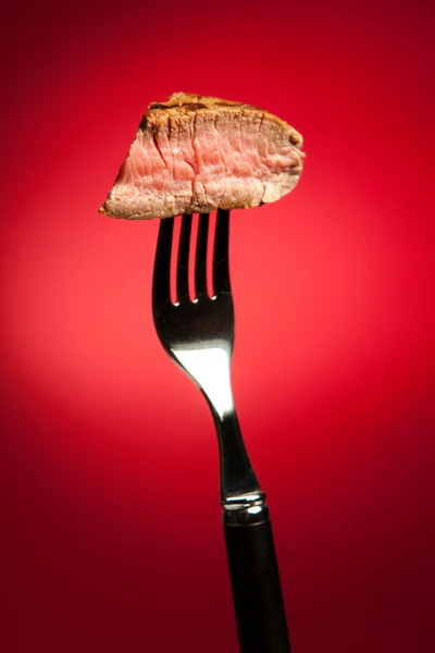 Piece of a grilled steak on a fork isolated on red — Stock Photo, Image