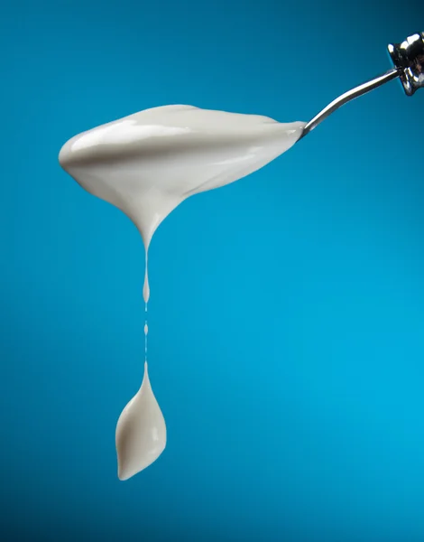 Spoon with yogurt on a blue background — Stock Photo, Image