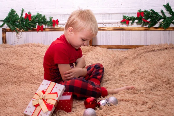 Slav bir çocuk 5 yıldır kırmızı giymiş, yatakta oturuyor. Çocuk yeni yıl hediyesinden memnun değil. Çocuk hediyeden rahatsız oldu.