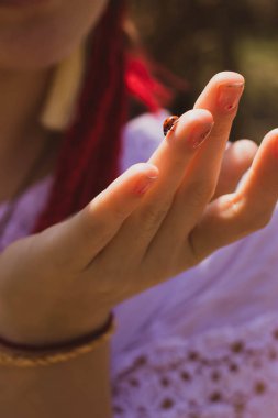 Kız elinde uğur böceği tutuyor.