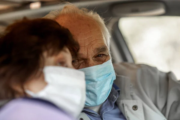 Tıbbi maske takmış yaşlı bir adam araba kullanıyor. Coronavirus salgını konsepti. Yolculuk, seyahat ve yaşlılar konsepti. Mutlu yaşlı çift araba kullanıyor.