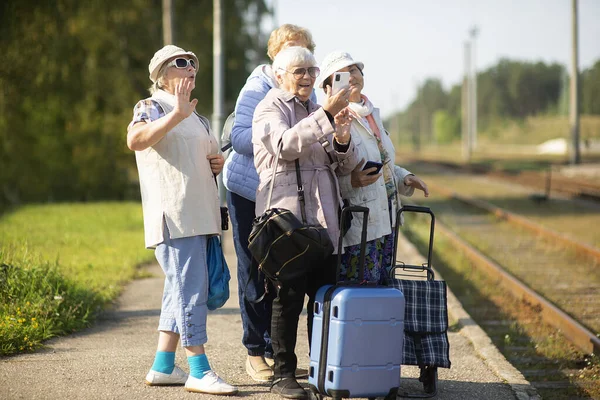 Group of smiling senior women take a self-portrait on a platform waiting for a train to travel during a COVID-19 pandemic