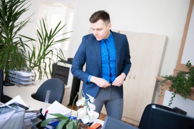 Büyük, modern bir ofiste tek başına çalışırken masaya yaslanan gülümseyen genç bir iş adamının portresi.