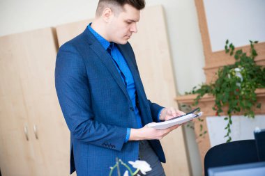 Modern ofiste hesap makinesi ve belge tutan genç bir işadamı.