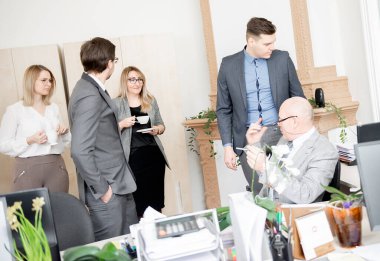 İş adamları modern ofiste çalışırken aletler kullanıyor, kahve içiyor, konuşuyor ve gülümsüyor.