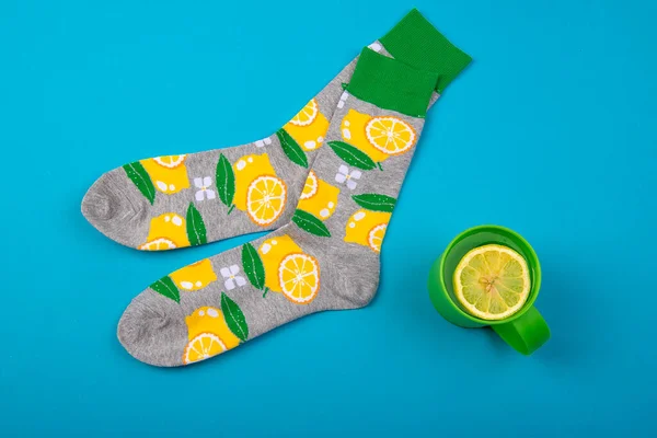 Renkli çoraplar ve limonlu çay fincanı mavi arka planda izole edilmiş turunçgil meyveleri.