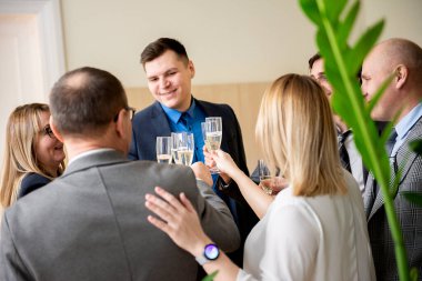 Başarılı iş adamları ofiste kutlama yaparken şampanya bardaklarını tokuşturup gülümsüyorlar.