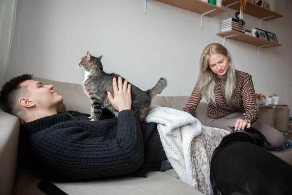 Young family couple with domestic cat and tea cup on sofa at home
