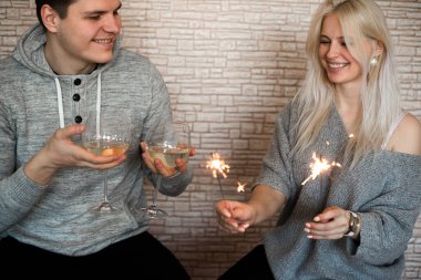 Şarap kadehleri ve maytapları olan genç mutlu çift yıldönümünü kutluyor ya da evde yeni yıl partisi veriyor.