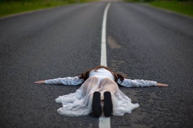 Beyaz elbiseli genç bir kadının, asfalt bir yolun beyaz çizgisi üzerinde uzanmış kollarını açmış dikiz aynasından.