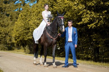 Açık hava düğün portresi. Güzel, çekici gelin, sevgilisi yakınlarda yürürken attan kurtuluyor..