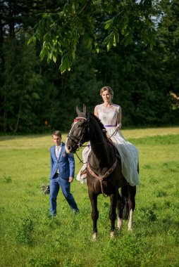 Açık hava düğün portresi. Güzel, çekici gelin, sevgilisi yakınlarda yürürken attan kurtuluyor..