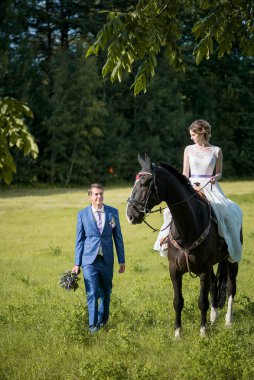 Açık hava düğün portresi. Güzel, çekici gelin, sevgilisi yakınlarda yürürken attan kurtuluyor..