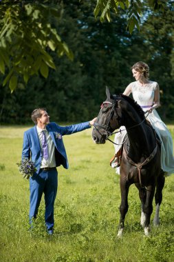 Açık hava düğün portresi. Güzel, çekici gelin, sevgilisi yakınlarda yürürken attan kurtuluyor..