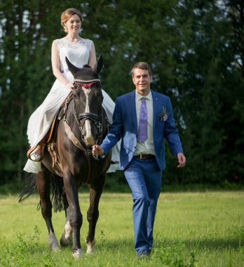 Açık hava düğün portresi. Güzel, çekici gelin, sevgilisi yakınlarda yürürken attan kurtuluyor..