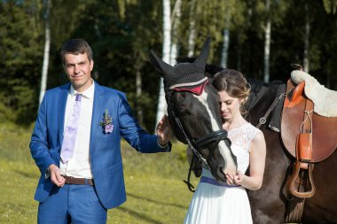 Yeni evli çift, doğada güzel büyük bir atla yaz güneşli bir günde ayakta duruyor.