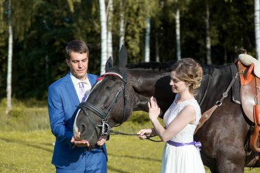 Yeni evli çift, doğada güzel büyük bir atla yaz güneşli bir günde ayakta duruyor.