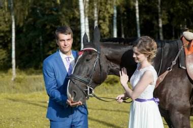 Yeni evli çift, doğada güzel büyük bir atla yaz güneşli bir günde ayakta duruyor.