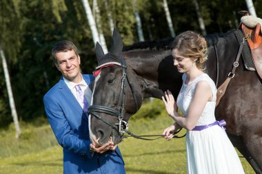 Yeni evli çift, doğada güzel büyük bir atla yaz güneşli bir günde ayakta duruyor.