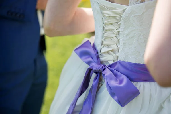 A close up of a wedding dress with a large purple silk bow