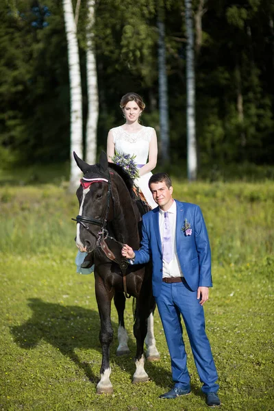 結婚式の屋外肖像画 彼女の恋人が近くを歩いている間 美しい魅力的な花嫁は馬に乗っています ロイヤリティフリーのストック写真
