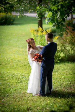 Düğün çifti yeşil çimlerde kucaklaşıyor, gelin kolunu damatların omuzlarında dinlendiriyor ve birbirlerine sıcak sevgi dolu bir bakış atıyorlar. .