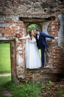 Genç gelin ve damat, eski bir taş pencere çerçevesinin içinde romantik bir evlilik imajı ve duygusal birliktelik oluşturan yumuşak bir öpücüğü paylaşıyor..