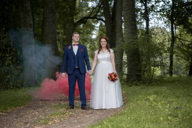 Gelin ve damat bir orman yolunda el ele yürürken kırmızı duman arkalarında sürükleniyor ve dramatik ve neşeli bir düğün sahnesi yaratıyor..