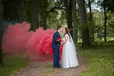 Genç gelin ve damat, renkli dumanlar ağaçların arasında kıvrılıp, barışçıl açık hava seremonisi anlarına kontrastlık ve duygu katarken şefkatli bir öpücük için duraklarlar..