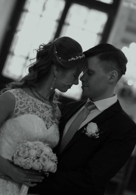 Kapalı alanda duran genç bir çiftin sanatsal siyah beyaz portresi. Yumuşak karşıtlık ve duygusal ifadeler dikey bir çerçevede zamansız romantizmi vurgular.