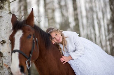 Gelin sıcak bir gülümseme ile ata doğru eğilir, yakınlık ve güveni ifade eder, ormanda samimi ve duygusal bir düğün portresi yaratır..