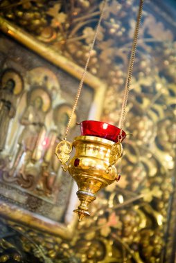 Zincirlerle süslenmiş altın kilise lambası, kırmızı cam bardak ve zengin dekoratif detaylarla dolu dini bir ikon içeriyor..
