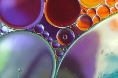 Petrol damlalarının soyut bir fotoğrafı suyun üzerinde yüzüyor.