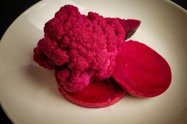 Pembe karnabahar ve beyaz bir tabakta dilimlenmiş pancar içeren canlı bir yemek.