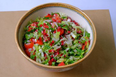 Dekoratif bir kasede renkli bir salata. İçinde marul, domates, nar tohumu ve otlar var.