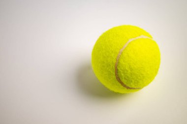 Beyaz arka planda parlak sarı bir tenis topu bulanık dokusunu ve karakteristik dikişlerini gösteriyor.