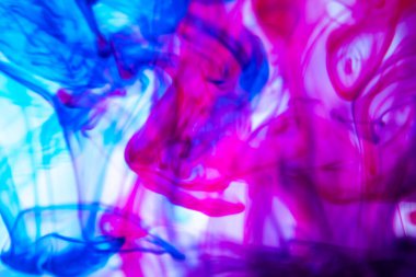 Suda dönen mavi ve pembe mürekkebin soyut görüntüsü.