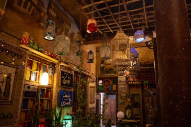 Tavandan sarkan renkli fenerler, sanat ve kültürel motiflerin yer aldığı dekore edilmiş duvarlar, yeşillik ekleyen bitkiler olan geleneksel bir restoran veya kafe.