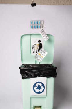 Siyah çantalı bir geri dönüşüm kutusu, yüzen hap paketleriyle çevrili bir geri dönüşüm sembolü ve alışveriş arabası olan bir kişinin grafiği.