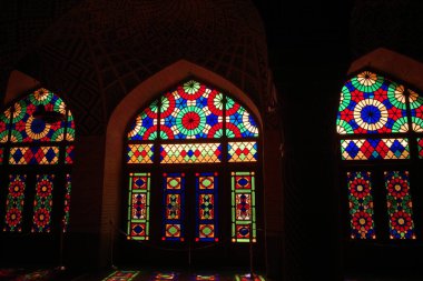 Mimari bir ortamda canlı vitraylı pencereler, karmaşık desenler ve renkli tasarımlar sergiliyor, tarihi bir binanın içine renkli ışıklar saçıyor.